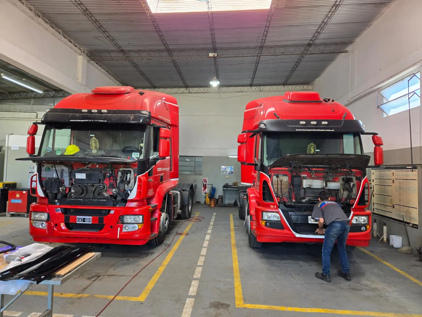 Dos tractoras Iveco de Transporte Colussi en servicio de mantenimiento preventivo, con los capós delanteros abiertos y un mecánico trabajando sobre una de ellas